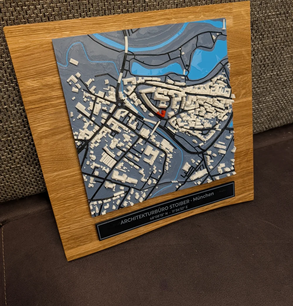 Farbiges 3D-Relief einer Altstadt mit Fluss auf einem Eichenbrett mit Naturkante, darunter ein Schild mit Namen und Koordinaten
