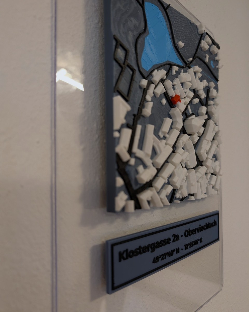 Farbiges 3D-Relief einer Kleinstadt mit Weiher auf einer klaren Acrylglasplatte an der Wand