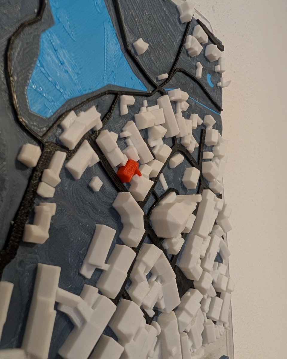 Farbiges 3D-Relief einer Kleinstadt mit Weiher auf einer klaren Acrylglasplatte an der Wand