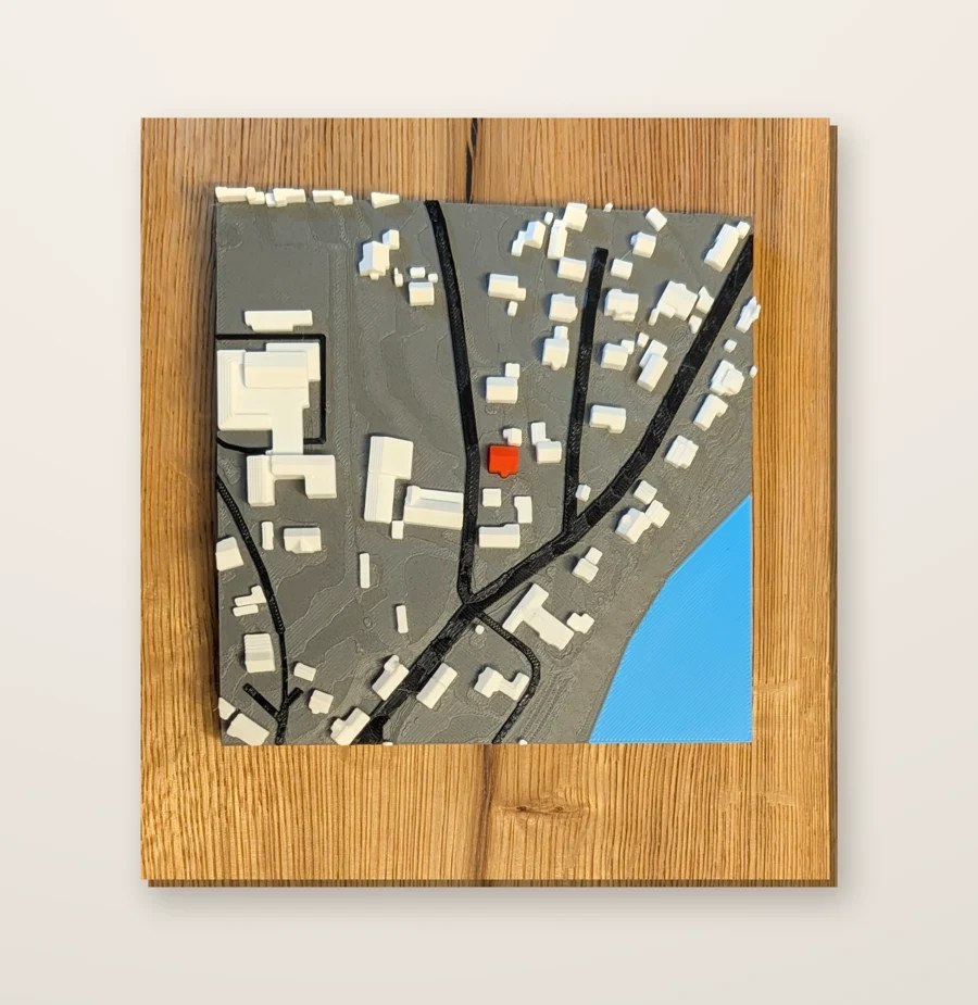 Farbiges 3D-Relief einer Wohnsiedlung mit markiertem Haus auf einem schlichten Eichenbrett